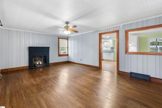 unfurnished living room featuring a brick fireplace, visible vents, crown molding, and wood finished floors