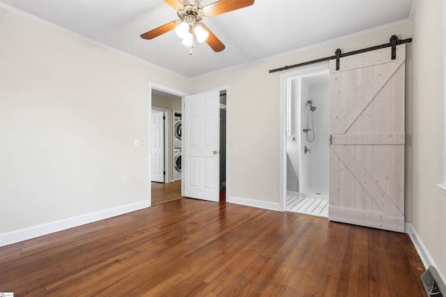 unfurnished bedroom with stacked washing maching and dryer, a barn door, visible vents, and hardwood / wood-style floors