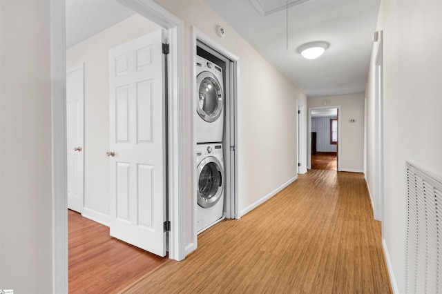 corridor with attic access, stacked washer / drying machine, visible vents, and light wood-style flooring