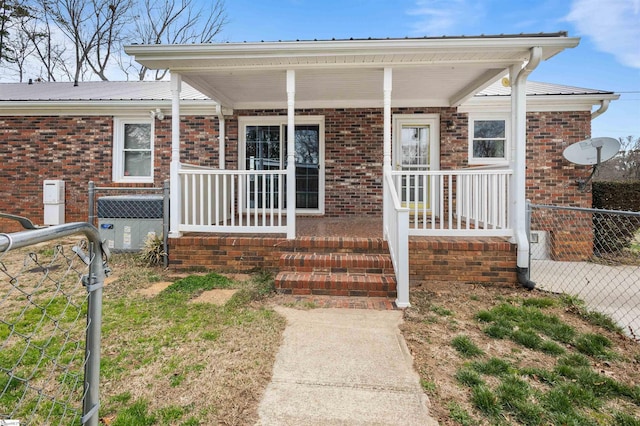 view of exterior entry featuring a porch, brick siding, metal roof, and fence