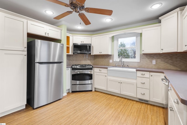 kitchen featuring light wood finished floors, tasteful backsplash, appliances with stainless steel finishes, white cabinets, and a sink