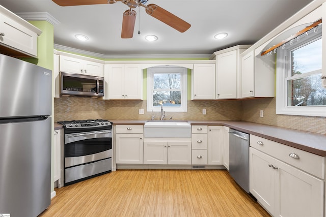 kitchen with stainless steel appliances, a sink, white cabinetry, light wood-type flooring, and decorative backsplash