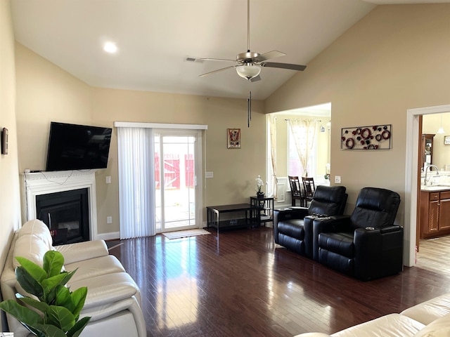 living room featuring visible vents, a ceiling fan, a glass covered fireplace, vaulted ceiling, and wood finished floors