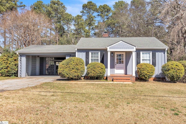 view of front of property with an attached carport, concrete driveway, board and batten siding, a chimney, and a front yard