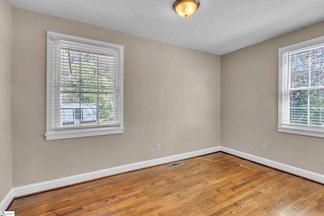 spare room with wood finished floors, visible vents, and baseboards