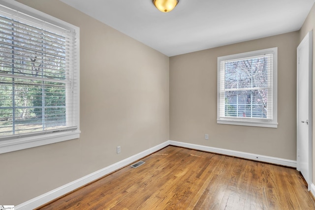 spare room with a healthy amount of sunlight, visible vents, hardwood / wood-style floors, and baseboards