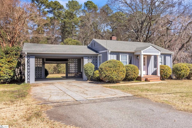 view of front of house featuring aphalt driveway, a front yard, a carport, board and batten siding, and a chimney