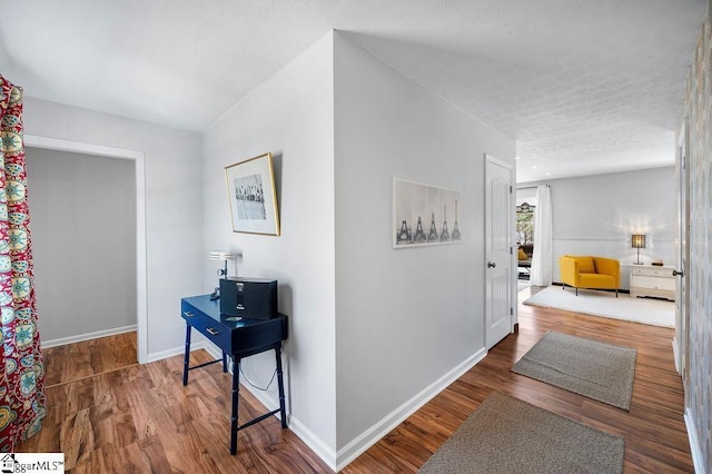 hallway with a textured ceiling, wood finished floors, and baseboards