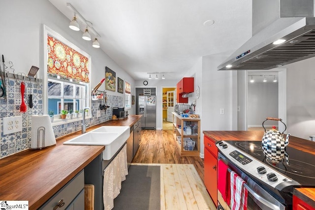 kitchen with stainless steel appliances, wooden counters, wall chimney range hood, and a sink