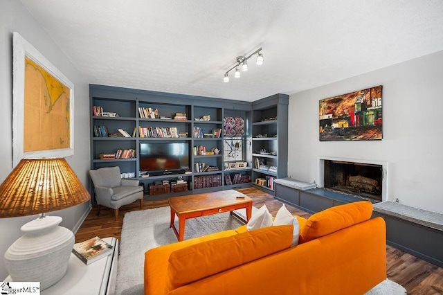 living room with built in shelves, a fireplace with raised hearth, a textured ceiling, and wood finished floors