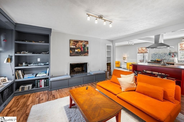 living room with built in features, a fireplace, a textured ceiling, and wood finished floors