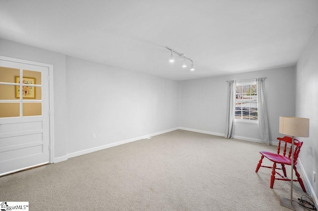 unfurnished room featuring rail lighting, carpet flooring, and baseboards