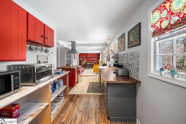 kitchen with hardwood / wood-style flooring, wood counters, red cabinets, range hood, and stainless steel microwave