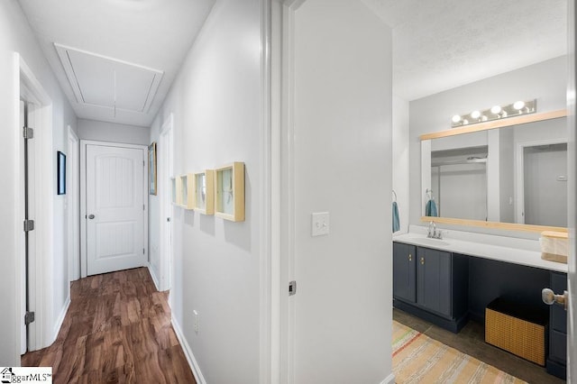 corridor with wood finished floors, a sink, attic access, and baseboards