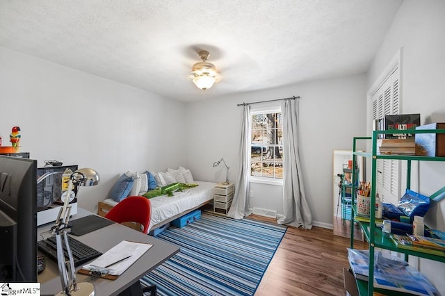 bedroom with a textured ceiling, wood finished floors, visible vents, and baseboards