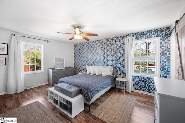 bedroom featuring a barn door, a textured ceiling, visible vents, and baseboards