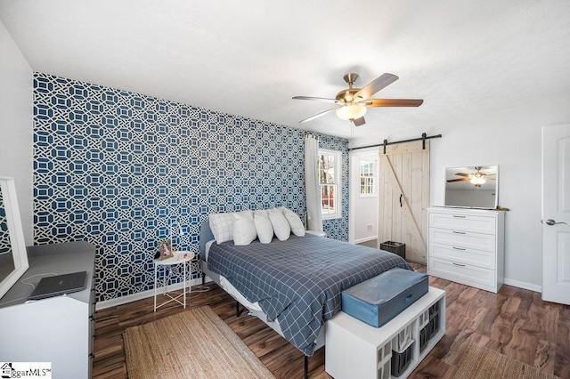 bedroom with ceiling fan, a barn door, wood finished floors, and baseboards