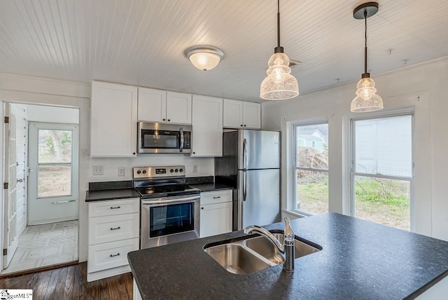 kitchen featuring dark wood finished floors, dark countertops, appliances with stainless steel finishes, white cabinets, and a sink