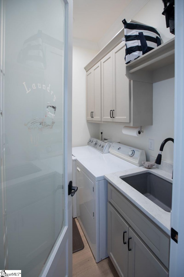 washroom with light wood-type flooring, independent washer and dryer, a sink, and cabinet space