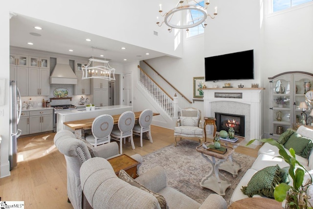 living room with stairway, a high ceiling, a glass covered fireplace, light wood-type flooring, and a chandelier