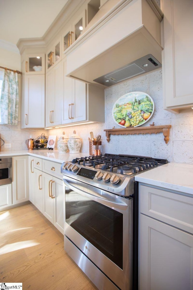 kitchen with light wood-type flooring, decorative backsplash, stainless steel range with gas stovetop, and custom range hood