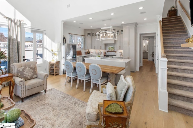 kitchen with light countertops, ornamental molding, stainless steel refrigerator with ice dispenser, light wood finished floors, and glass insert cabinets