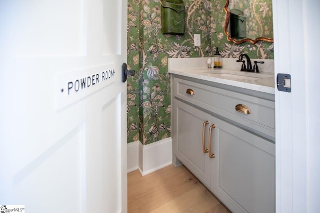 bathroom with wallpapered walls, wood finished floors, and vanity