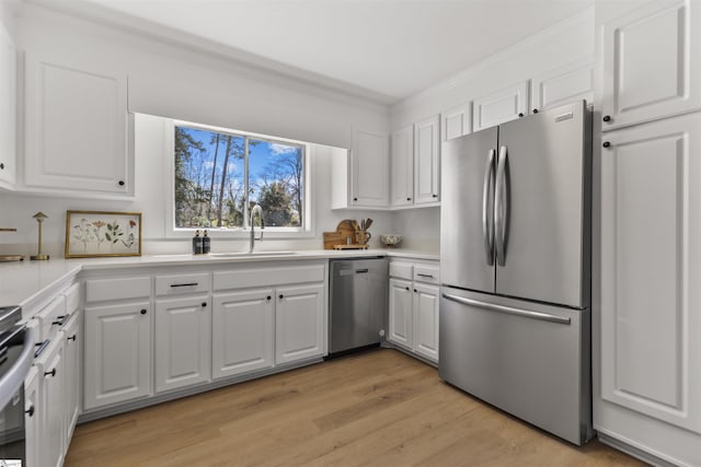 kitchen with light wood finished floors, stainless steel appliances, light countertops, white cabinetry, and a sink