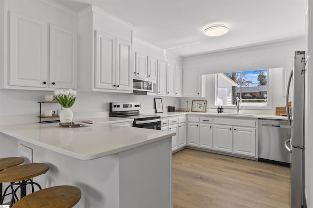 kitchen with a breakfast bar area, a peninsula, a sink, white cabinetry, and appliances with stainless steel finishes