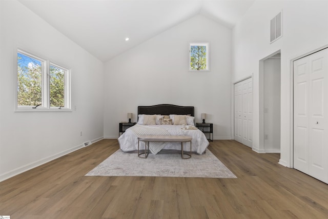 bedroom with visible vents, multiple windows, high vaulted ceiling, and wood finished floors