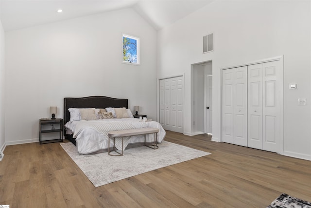 bedroom featuring baseboards, visible vents, wood finished floors, high vaulted ceiling, and multiple closets