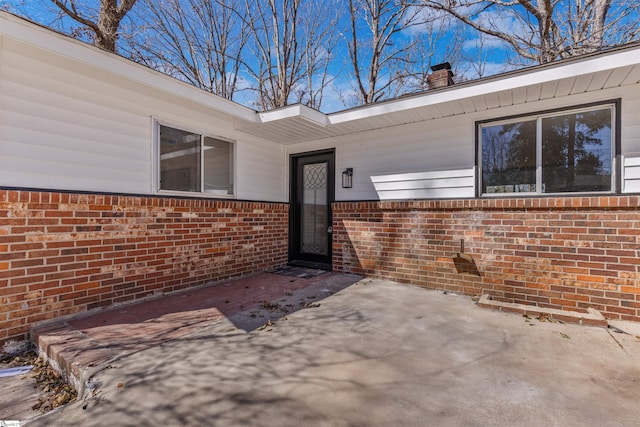 view of exterior entry featuring a patio area, brick siding, and a chimney