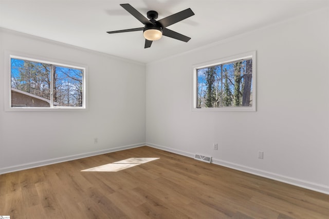 empty room with visible vents, plenty of natural light, baseboards, and wood finished floors