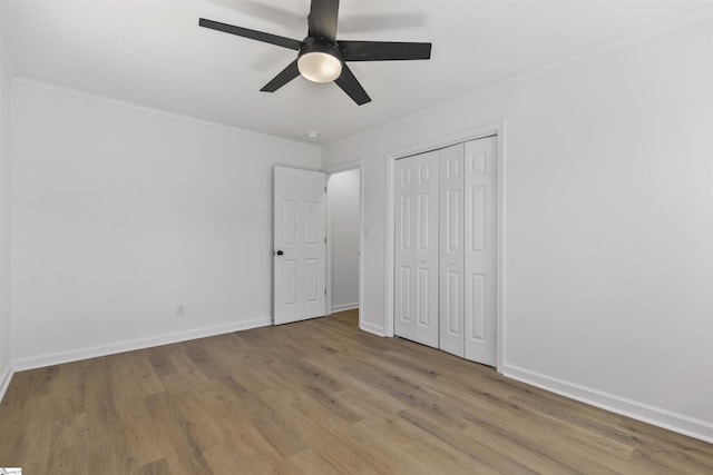 unfurnished bedroom with baseboards, a closet, wood finished floors, and crown molding