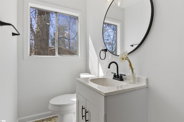 half bath with toilet, a healthy amount of sunlight, baseboards, and vanity