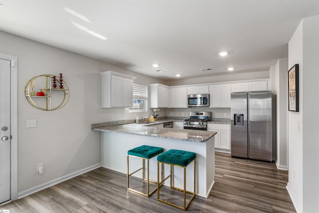 kitchen with a peninsula, appliances with stainless steel finishes, a sink, and white cabinets