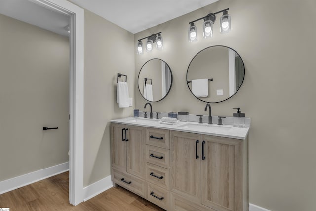 full bathroom with double vanity, baseboards, a sink, and wood finished floors