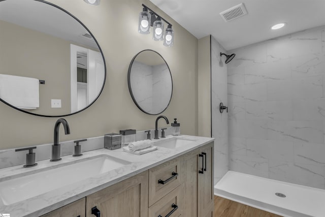 bathroom with visible vents, a sink, a tile shower, and double vanity