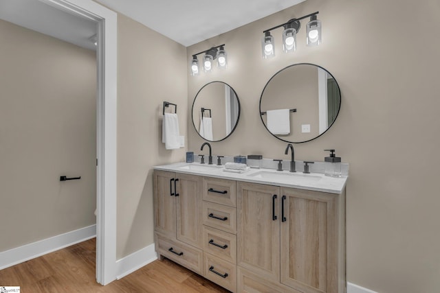 bathroom with double vanity, baseboards, a sink, and wood finished floors