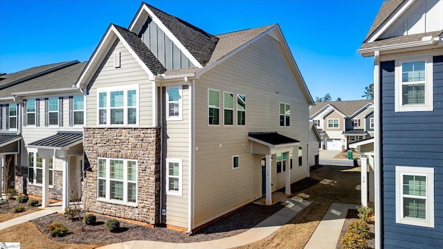 view of home's exterior featuring a shingled roof, stone siding, board and batten siding, a residential view, and a standing seam roof