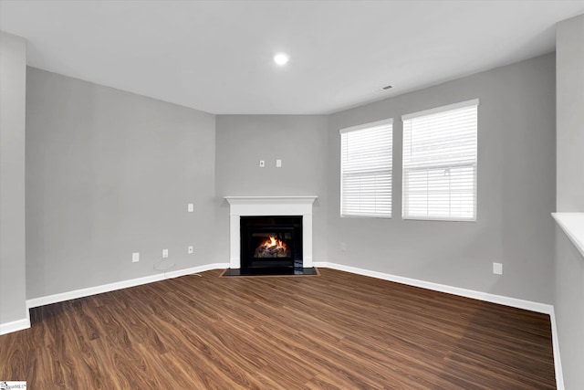 unfurnished living room with dark wood-style flooring, a fireplace with flush hearth, and baseboards