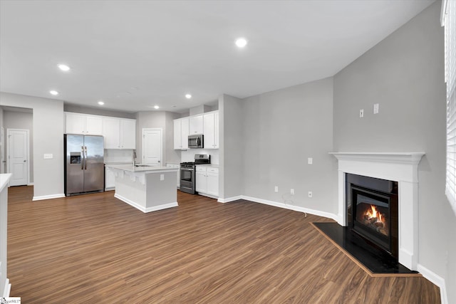 kitchen with dark wood-type flooring, white cabinets, open floor plan, appliances with stainless steel finishes, and a glass covered fireplace