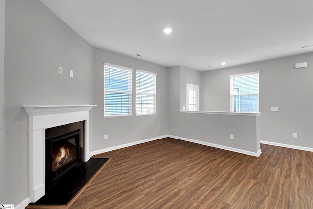 unfurnished living room featuring a warm lit fireplace, plenty of natural light, baseboards, and dark wood-style flooring