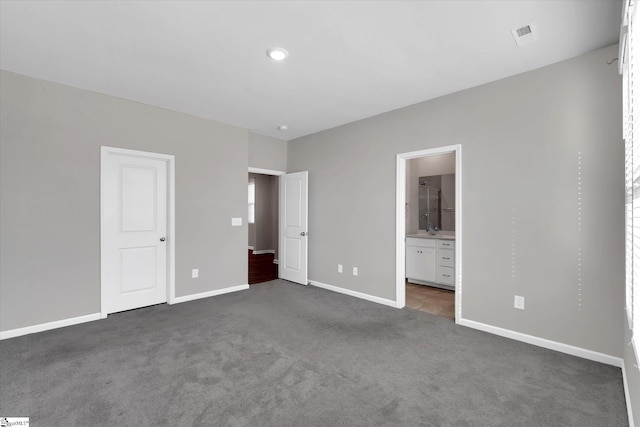 unfurnished bedroom featuring baseboards, dark carpet, and connected bathroom