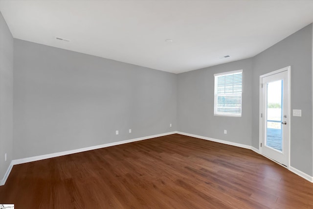 unfurnished room with dark wood-style flooring, visible vents, and baseboards