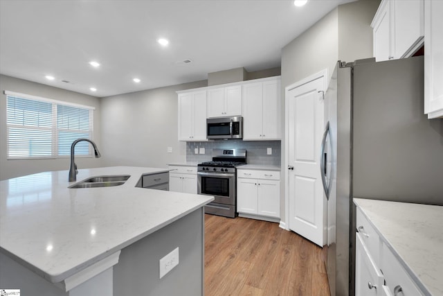 kitchen featuring a sink, appliances with stainless steel finishes, decorative backsplash, light wood finished floors, and an island with sink