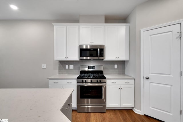 kitchen featuring stainless steel appliances, wood finished floors, white cabinetry, and tasteful backsplash