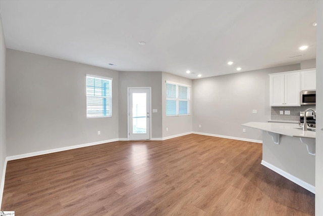 kitchen featuring light countertops, light wood-type flooring, backsplash, stainless steel microwave, and a kitchen bar