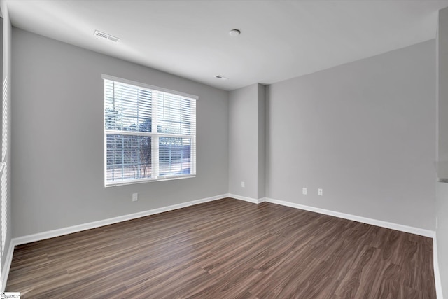 empty room featuring dark wood-style flooring, visible vents, and baseboards