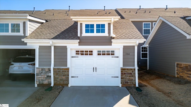 exterior space with driveway, stone siding, roof with shingles, and an attached garage